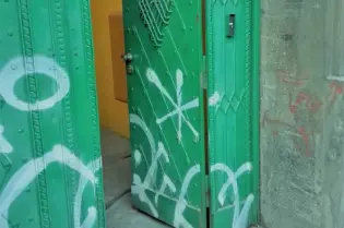Zielone drzwi z graffiti, częściowo otwarte, prowadzące do wnętrza.
