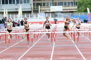 Biegaczki pokonujące przeszkody na torze lekkoatletycznym.