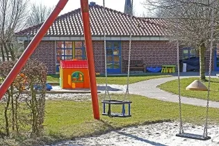 Plac zabaw z huśtawkami, domkiem dla dzieci i ścieżką w otoczeniu zieleni.