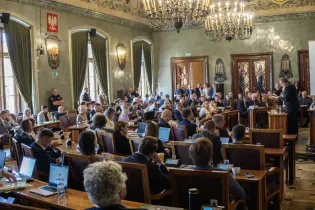 Debata w sali obrad z uczestnikami i mówcą na podium.
