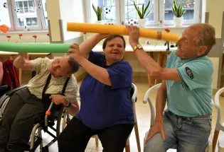 Trzy osoby bawią się w pomieszczeniu, używając kolorowych rur jako rekwizytów.