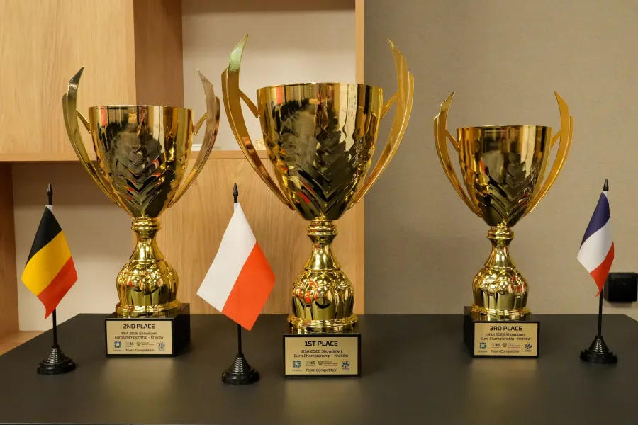 Trzy złote trofea z flagami Belgii, Polski i Francji.