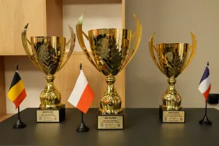 Trzy złote trofea z flagami Belgii, Polski i Francji.