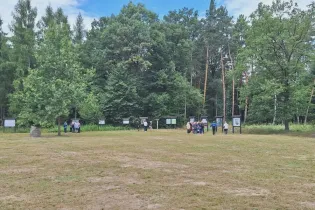 Grupa ludzi w lesie, oglądająca tablice informacyjne.