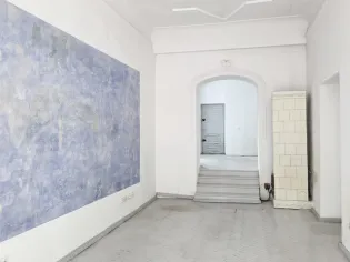 Pusty, jasny pokój z niebieską ścianą i drzwiami prowadzącymi do innego pomieszczenia.