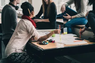 Grupa osób pracujących nad projektem przy stole, z kolorowymi markerami i notatkami.