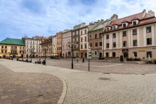 Rynek z kolorowymi kamienicami i brukowanymi alejkami. Spokojna atmosfera z kilkoma przechodniami.
