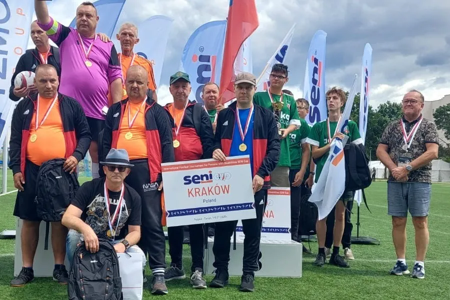 Grupa sportowców na podium z medalami, trzymających tabliczkę z napisem Kraków.