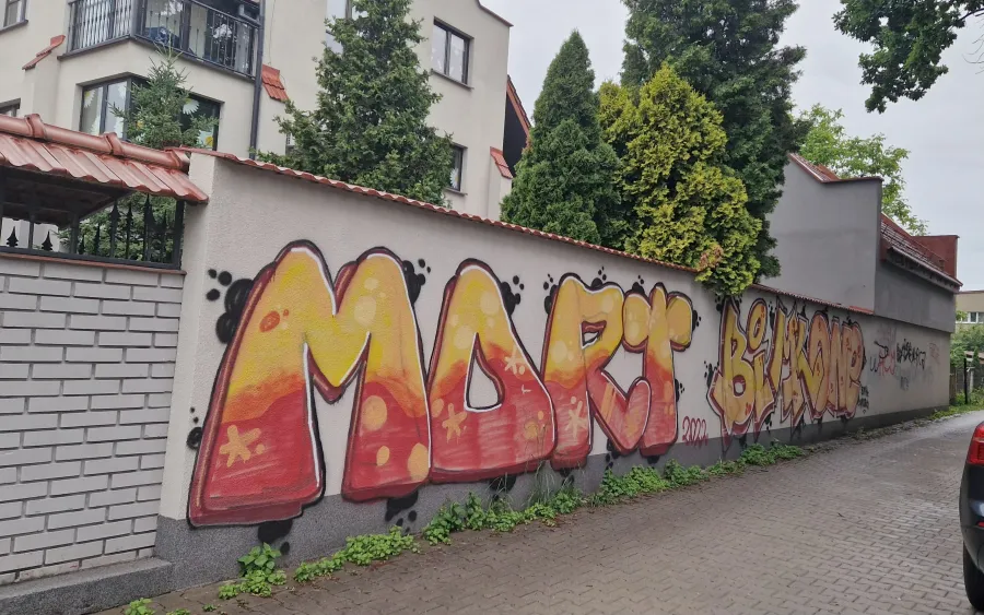 Graffiti na murze z napisem "MORC" w kolorach pomarańczowym i żółtym.