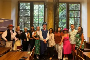 Na zdjęciu grupa osób pozująca na tle okna w zabytkowej sali. Kilkoro z nich to członkowie folklorystycznego zespołu polonijnego z San Francisco "Łowiczanie" i są ubrani w ludowe stroje łowickie 