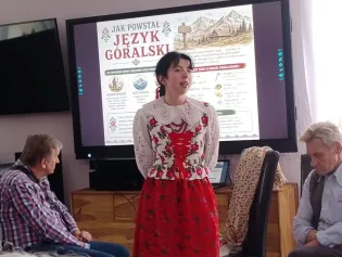 Kobieta w tradycyjnym stroju góralskim prezentuje informacje o języku góralskim.