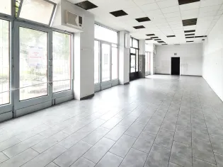 Pusty lokal z dużymi oknami i szarym kafelkowym podłogą.