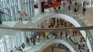 Ludzie poruszający się po nowoczesnym wnętrzu z spiralnymi schodami i dużymi oknami.