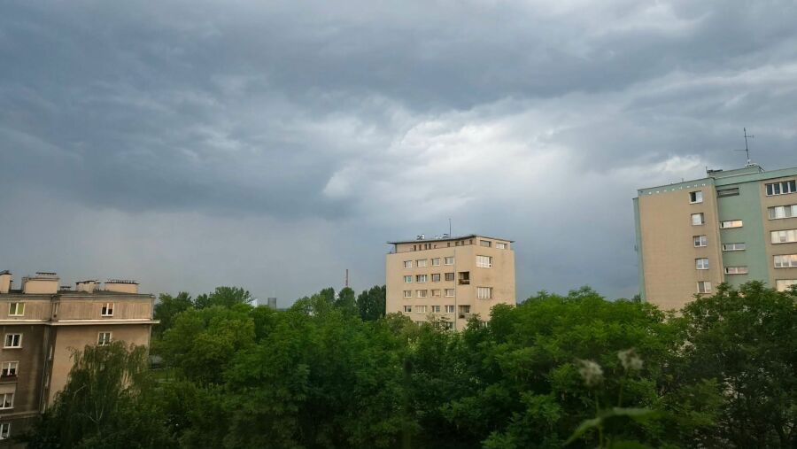 Widać zachmurzane nieb nad blokami i koronami drzew.