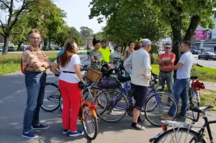 Grupa rowerzystów rozmawia na ścieżce rowerowej, w tle ruch uliczny.