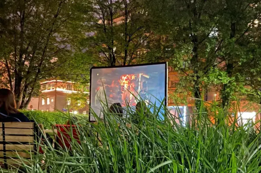 Kino plenerowe z ekranem wyświetlającym film, otoczone zielenią i drzewami.