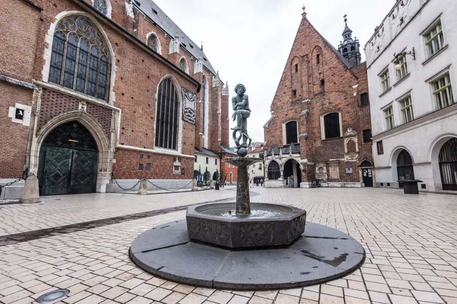 Fontanna z rzeźbą w centrum placu otoczonego historycznymi budynkami.