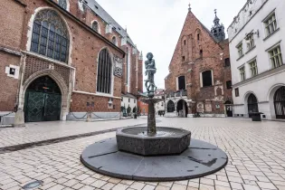 Fontanna z rzeźbą w centrum placu otoczonego historycznymi budynkami.