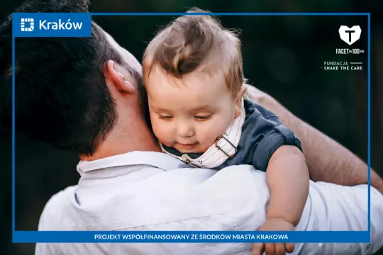 Mężczyzna trzyma na rękach małe dziecko, oboje uśmiechnięci.