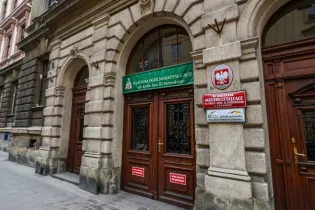Budynek szkoły z tablicą informacyjną i herbem Polski.