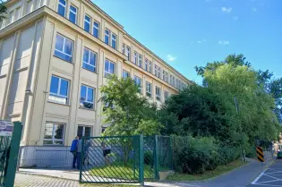 Budynek z dużymi oknami otoczony zielenią, widok z ulicy.