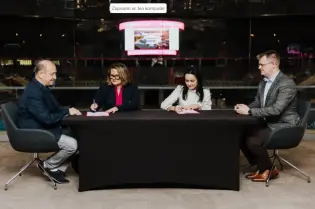 Cztery osoby przy stole podpisują dokumenty w nowoczesnym otoczeniu.