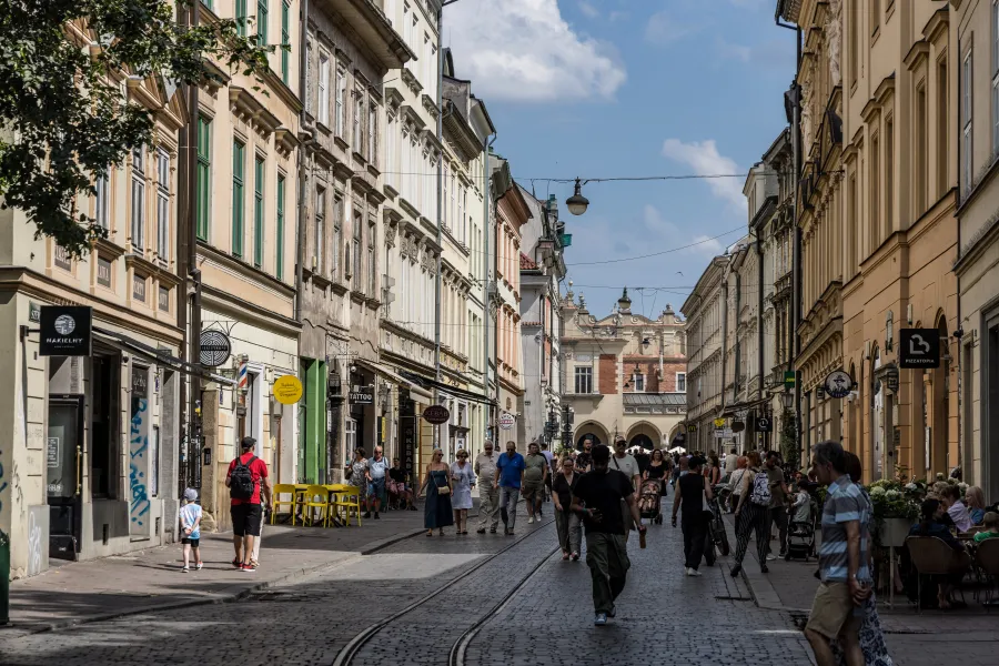 Ulica z kolorowymi kamienicami, ludzie spacerujący i kawiarnie na chodniku.