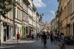 Ulica z kolorowymi kamienicami, ludzie spacerujący i kawiarnie na chodniku.