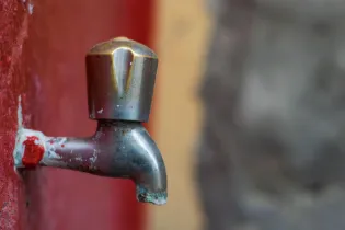 Kran w kolorze metalicznym na tle czerwonej ściany.