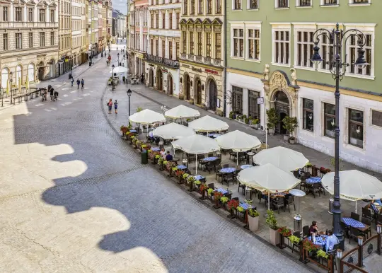 Urokliwa ulica z kawiarniami i parasolami, otoczona zabytkowymi budynkami.