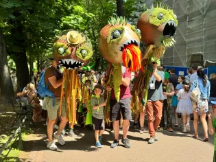 Grupa osób niosących duże, kolorowe maski w kształcie potworów podczas parady.