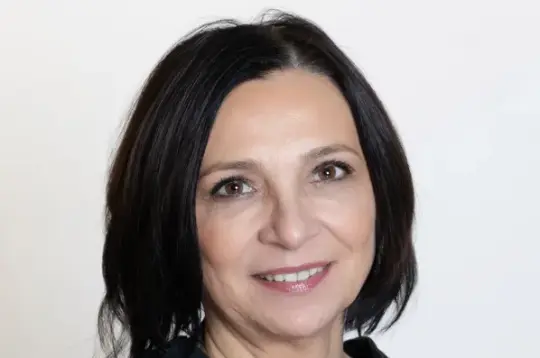 Kobieta w czarnej bluzce, z krótkimi włosami, uśmiecha się do kamery.