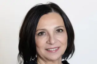 Kobieta w czarnej bluzce, z krótkimi włosami, uśmiecha się do kamery.