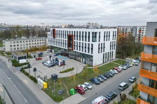 Nowoczesny budynek biurowy z parkingiem i otoczeniem miejskim.