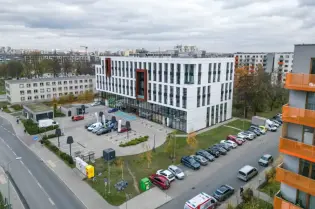 Nowoczesny budynek biurowy z parkingiem i otoczeniem miejskim.
