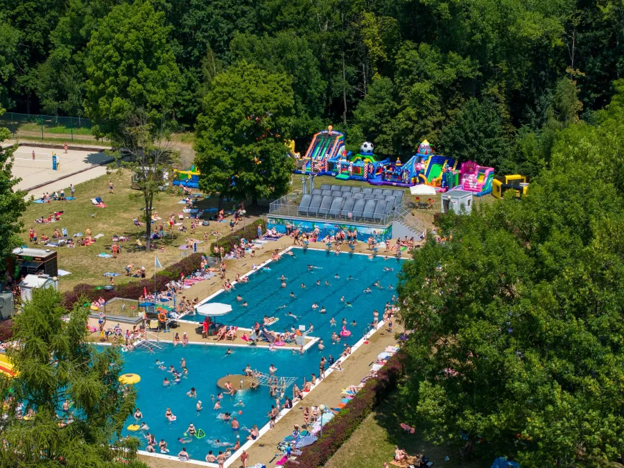 Basen z atrakcjami wodnymi, zjeżdżalniami i plażą, pełen ludzi w letniej scenerii.