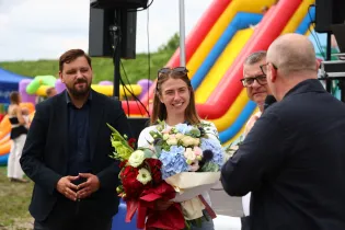 Kobieta z bukietem kwiatów rozmawia z mężczyznami na tle kolorowych zjeżdżalni.