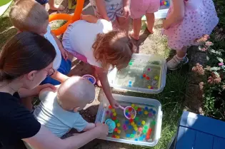 Dzieci bawią się w wodzie, łowią kolorowe kulki za pomocą sitka.