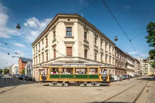 Zabytkowy tramwaj na ulicy w mieście, otoczony budynkami i samochodami.