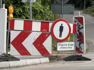 Znak drogowy z informacją o przejściu dla pieszych i wskazówką do przejścia na drugą stronę ulicy.