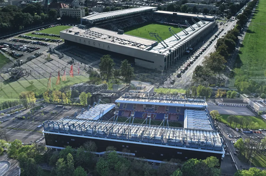 Widok na stadion i otaczający go teren, z zielonymi przestrzeniami i budynkami w tle.