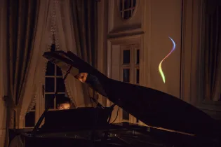 Muzyk grający na fortepianie w eleganckim wnętrzu z kolorowym światłem na ścianie.