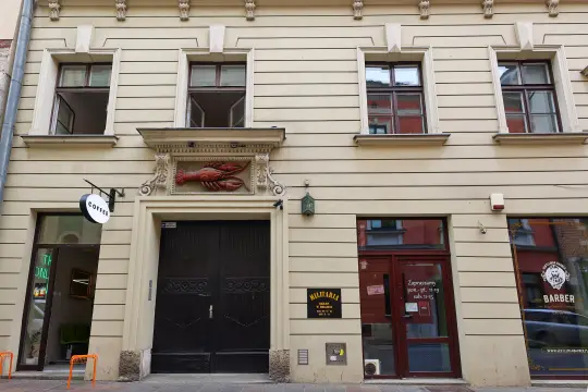 Kamienica z rzeźbą homara nad wejściem, obok lokale gastronomiczne i fryzjerskie.