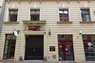 Kamienica z rzeźbą homara nad wejściem, obok lokale gastronomiczne i fryzjerskie.
