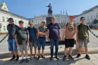 Grupa mężczyzn pozująca przed pomnikiem w słoneczny dzień.