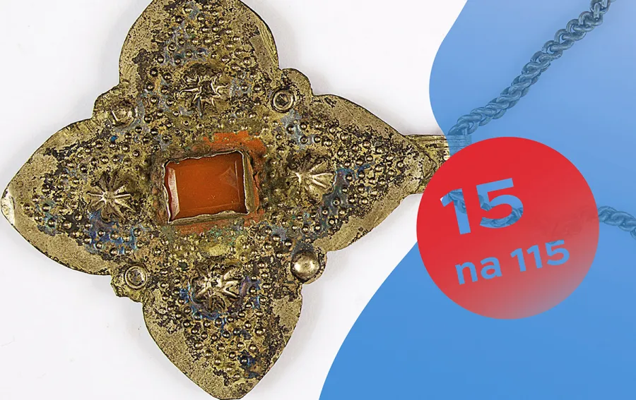 Złoty wisiorek w kształcie kwadratu z czerwonym kamieniem w środku.