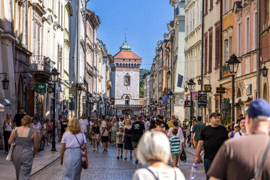 liczne osoby idą pojedynczo ulicą Floriańską w Krakowie. Tłum przechodniów widać od tyłu na tle oddalonej ceglanej Bramy Floriańskiej.    