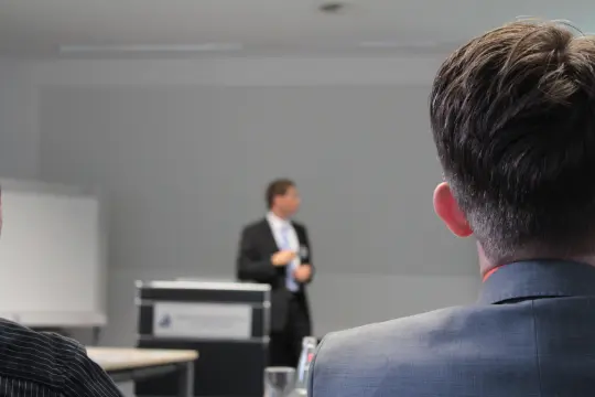 Uczestnicy wykładu słuchają prelegenta stojącego przy mównicy w sali konferencyjnej.