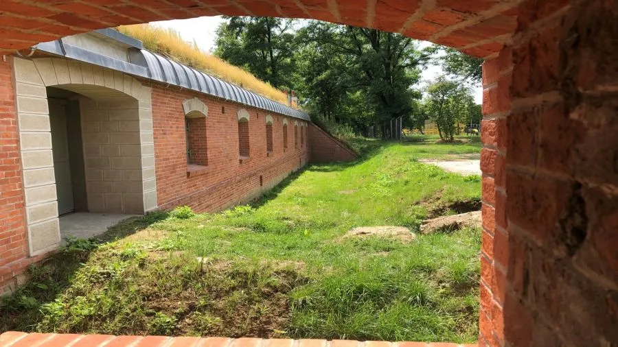 Widok na ceglaną budowlę z zielonym dachem i otaczającą ją trawę.