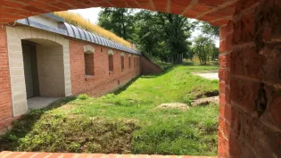 Widok na ceglaną budowlę z zielonym dachem i otaczającą ją trawę.